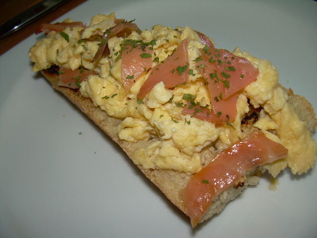 Rebanada de pan con huevos revueltos y salmón ahumado sobre un plato blanco